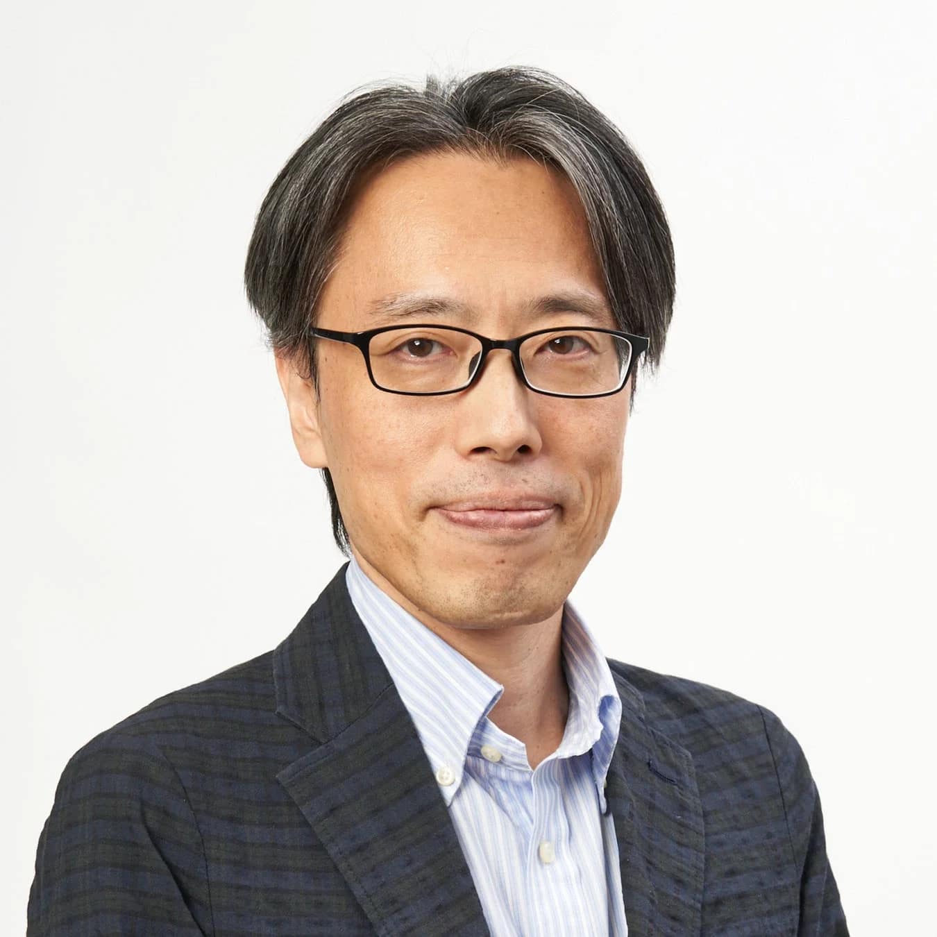 白い背景を背にした、眼鏡をかけたアジア系男性のポートレート。グレーの混じった髪とストライプのシャツ、柄物のジャケットを着用し、穏やかな表情をしています。