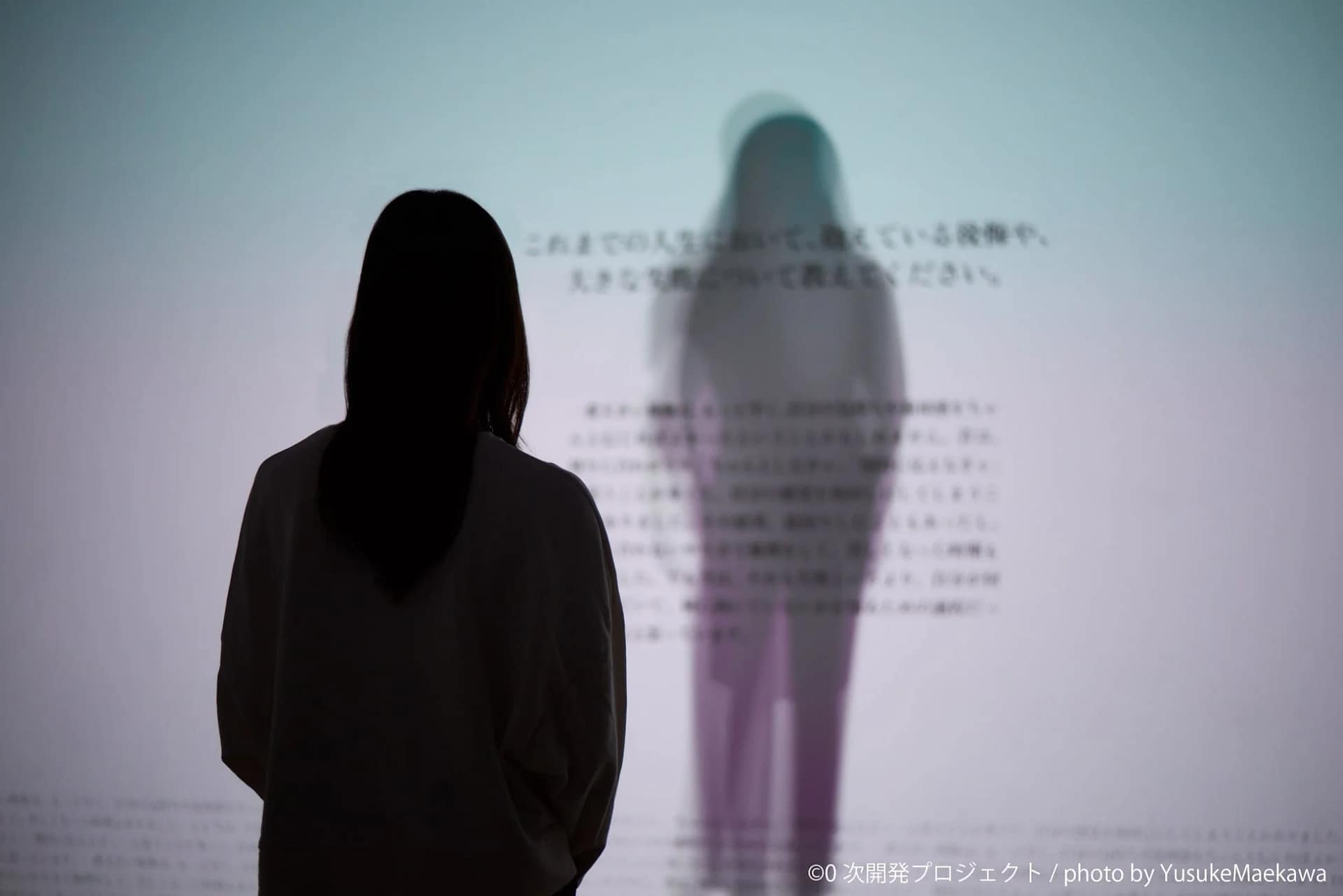 壁に投影されたテキストとぼやけた人影を見つめる人物のシルエット