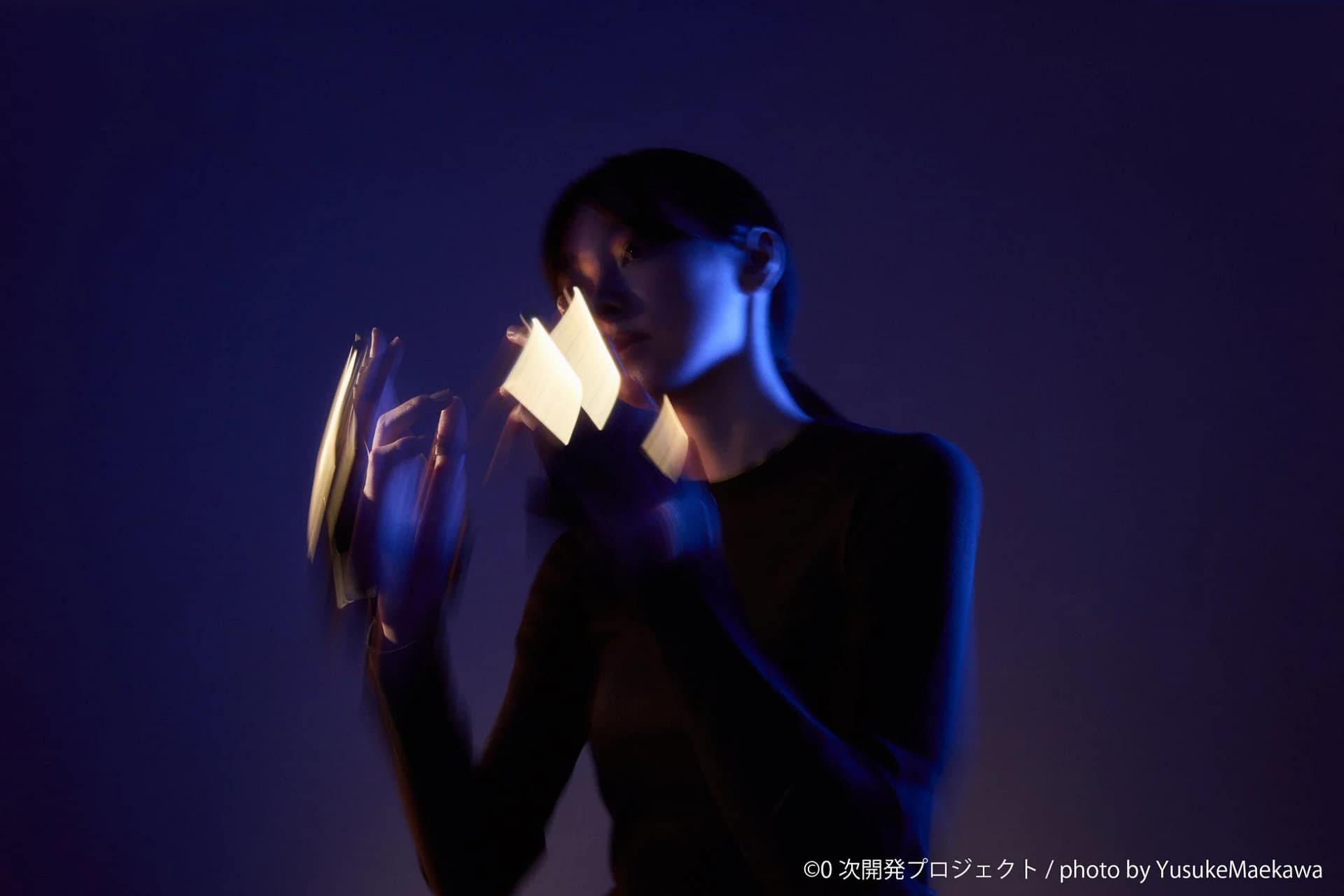 青い光に照らされた女性が発光する物体を両手で持っている様子