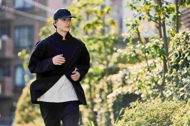 黒いキャップとジャケットを着用した男性が、ワイヤレスイヤホンを付けて屋外でジョギングしている様子です。