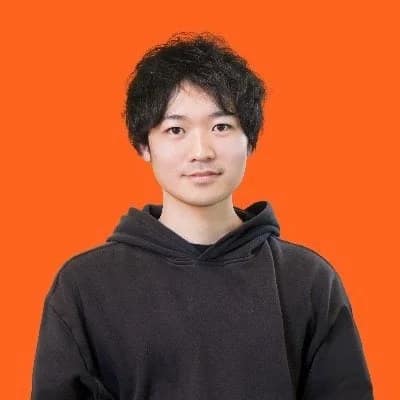 オレンジ色の背景を背に、黒いパーカーを着た若い日本人男性のポートレート写真です。男性はカメラをまっすぐ見ており、穏やかな表情をしています。